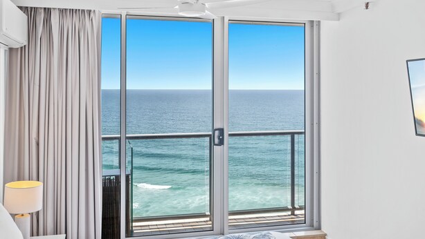 Un dormitorio con un amplio ventanal corredera que da a un balcón con vistas al océano.
