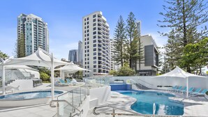 Un área de piscina en la azotea con sillones de descanso, barandilla de cristal y vista despejada de edificios altos circundantes.