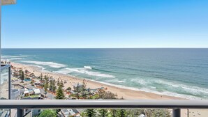 Vista costera desde un balcón con vistas a una playa, edificios y árboles.