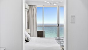 Habitación de hotel con una cama, una silla, un ventilador de techo y vista al océano a través de puertas correderas amplias.