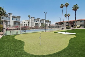 A golf course with a putting green, palm trees, and a building with a red roof.