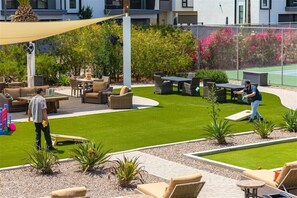 A well-maintained outdoor patio area with seating arrangements, a lawn, and a tennis court in the background. - 211 Fully Furnished 1BR Suite-Heated Pool! (Scottsdale)