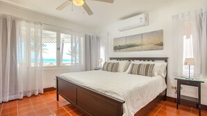 Ein Schlafzimmer mit Bett, Deckenventilator, Fenster mit Vorhängen, Nachttisch und Wandklimaanlage.