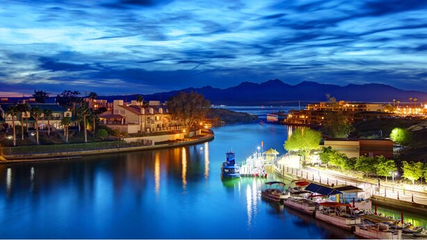 A riverside town with a calm river, boats docked along the shore, and buildings with lights on. - Sleeps 23: Luxury Retreat with Pool/Hot Tub, Casitas, Pet-Friendly, Near Riviera Marina (Lake Havasu City)