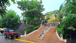 A red SUV parked on a wet road with a staircase leading to a building. - PRIVATE ROOFTOP, HILLTOP PANORAMIC OCEAN-VIEW CONDO. COCO SUNSET HILLS, CR. (playas del coco)