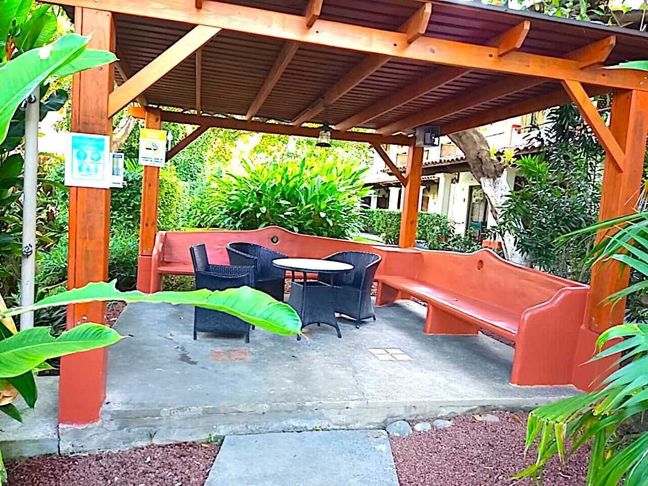 En utomhusplats med sittmöbler, bestående av en träpergola, ett bord och två stolar.