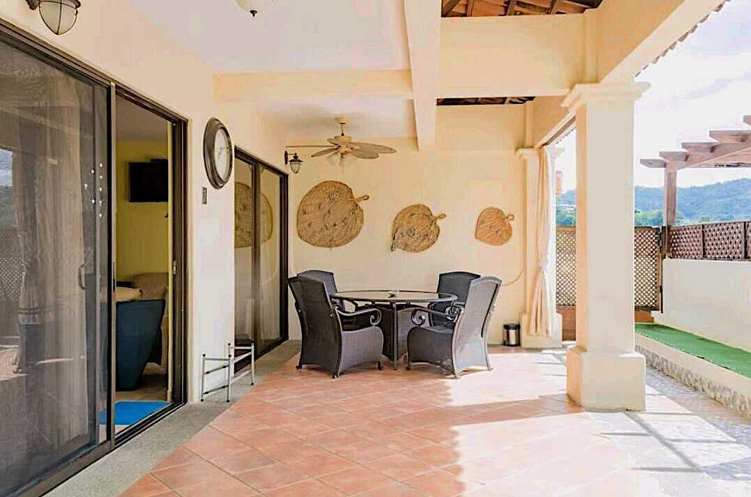 Une terrasse extérieure avec une table et des chaises, un ventilateur de plafond et des éléments décoratifs sur les murs.