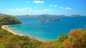 A coastal landscape with a beach, clear blue sea, and distant islands. - PRIVATE ROOFTOP, HILLTOP PANORAMIC OCEAN-VIEW CONDO. COCO SUNSET HILLS, CR. (playas del coco)