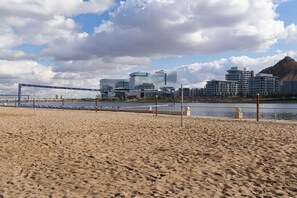 Enjoy beach activities like volleyball in a coastal area with modern urban surroundings.