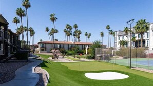 Ein gepflegter Golfplatz mit klarem Weg, Palmen und modernen Gebäuden im Hintergrund.