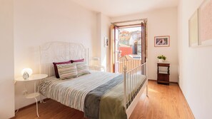 A bedroom with a bed, bedside table, lamp, and a view of the outside.