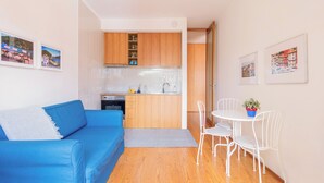 Un espace de vie compact comprenant un coin cuisine, un canapé bleu, une table à manger avec des chaises et des œuvres d’art accrochées aux murs.