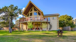 A two-story house with a balcony, a small porch, and a fenced yard. - LAURA’S LODGE – BEAUTIFUL RIVER, KAYAKS, TUBES, HOT TUB - WELCOME! (Wimberley)