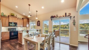 A spacious kitchen with wooden cabinets, a dining area with a table and chairs, and a view of a lush landscape through large sliding glass doors. - LAURA’S LODGE – BEAUTIFUL RIVER, KAYAKS, TUBES, HOT TUB - WELCOME! (Wimberley)