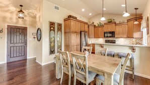 A spacious kitchen with wooden cabinets, a large dining table, and pendant lighting. - LAURA’S LODGE – BEAUTIFUL RIVER, KAYAKS, TUBES, HOT TUB - WELCOME! (Wimberley)