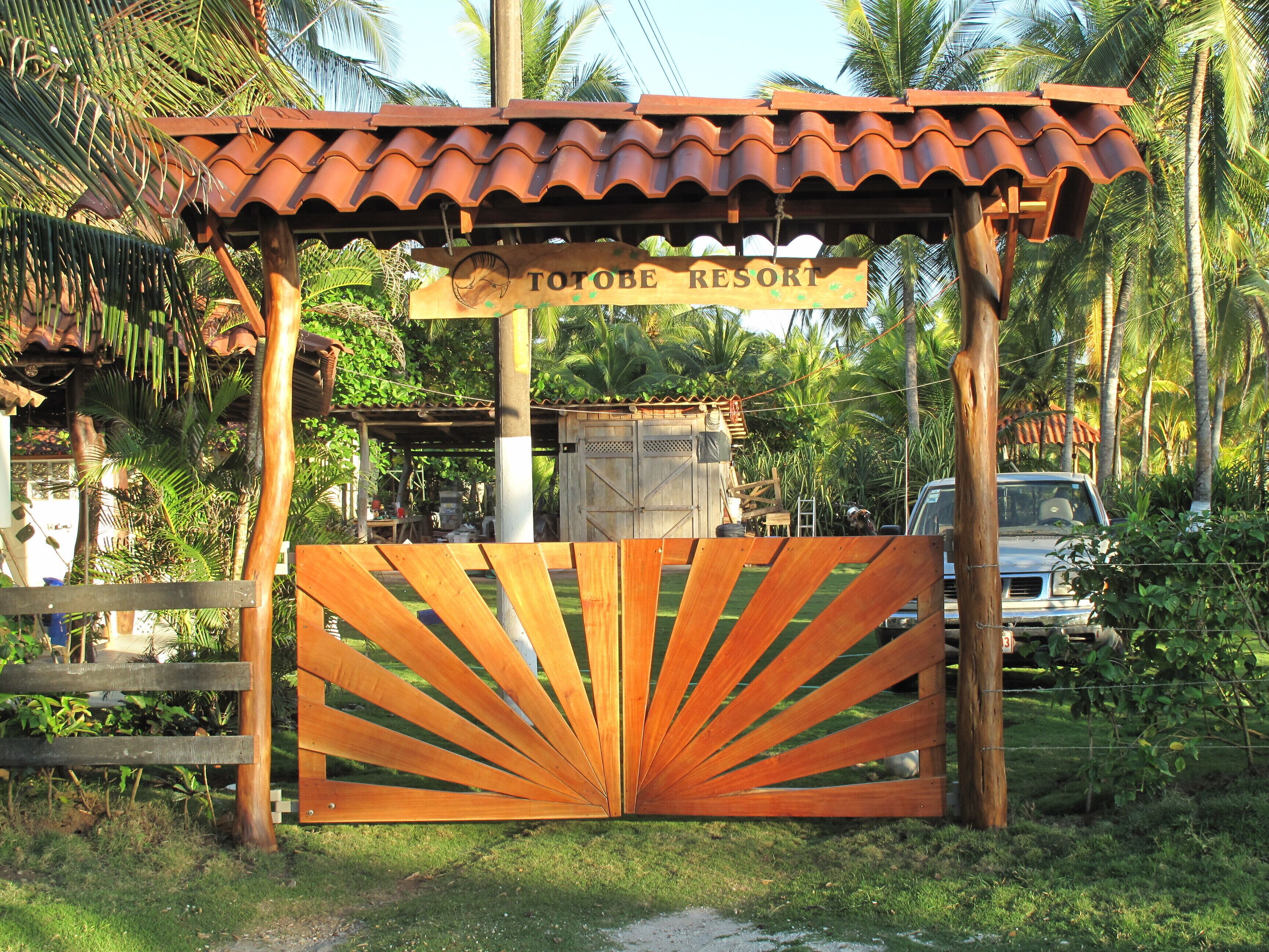 Een houten poort met een bord waarop 'TOTOBE RESORT' staat, voor een gebouw met een pannendak.