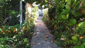 Ein schmaler Steinweg, gesäumt von üppigem Grün und einem Gebäude mit dunkler Fassade.