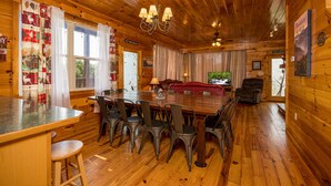 A wooden cabin interior with a dining area, kitchen, and living room. - Smoky Mountain Lodge | 6 King Suites, Hot Tub, Views, Game Room, flat entry (Sevierville)