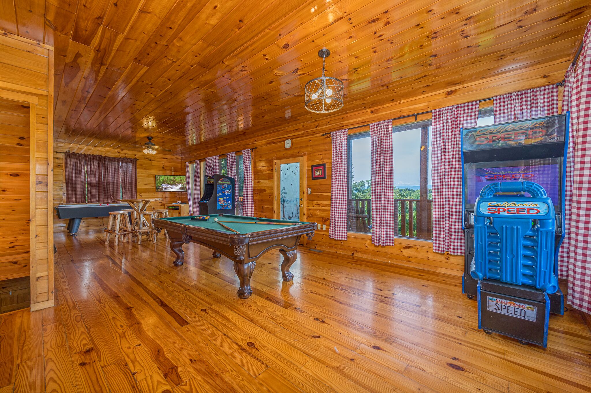 A wooden interior with a pool table, a pinball machine, and a billiards table.
