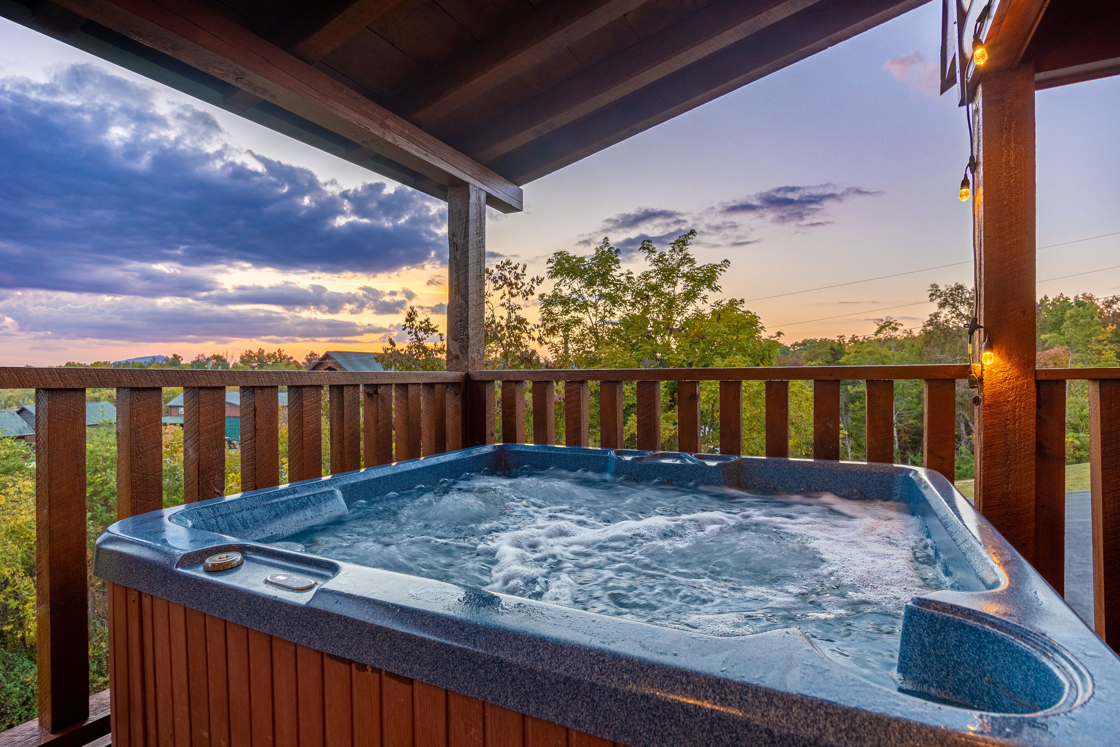 A hot tub on a wooden deck with a view of trees and a cloudy sky.