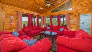 A cozy cabin with a wooden interior, red sofas, a ceiling fan, and a view of the outdoors. - Smoky Mountain Lodge | 6 King Suites, Hot Tub, Views, Game Room, flat entry (Sevierville)