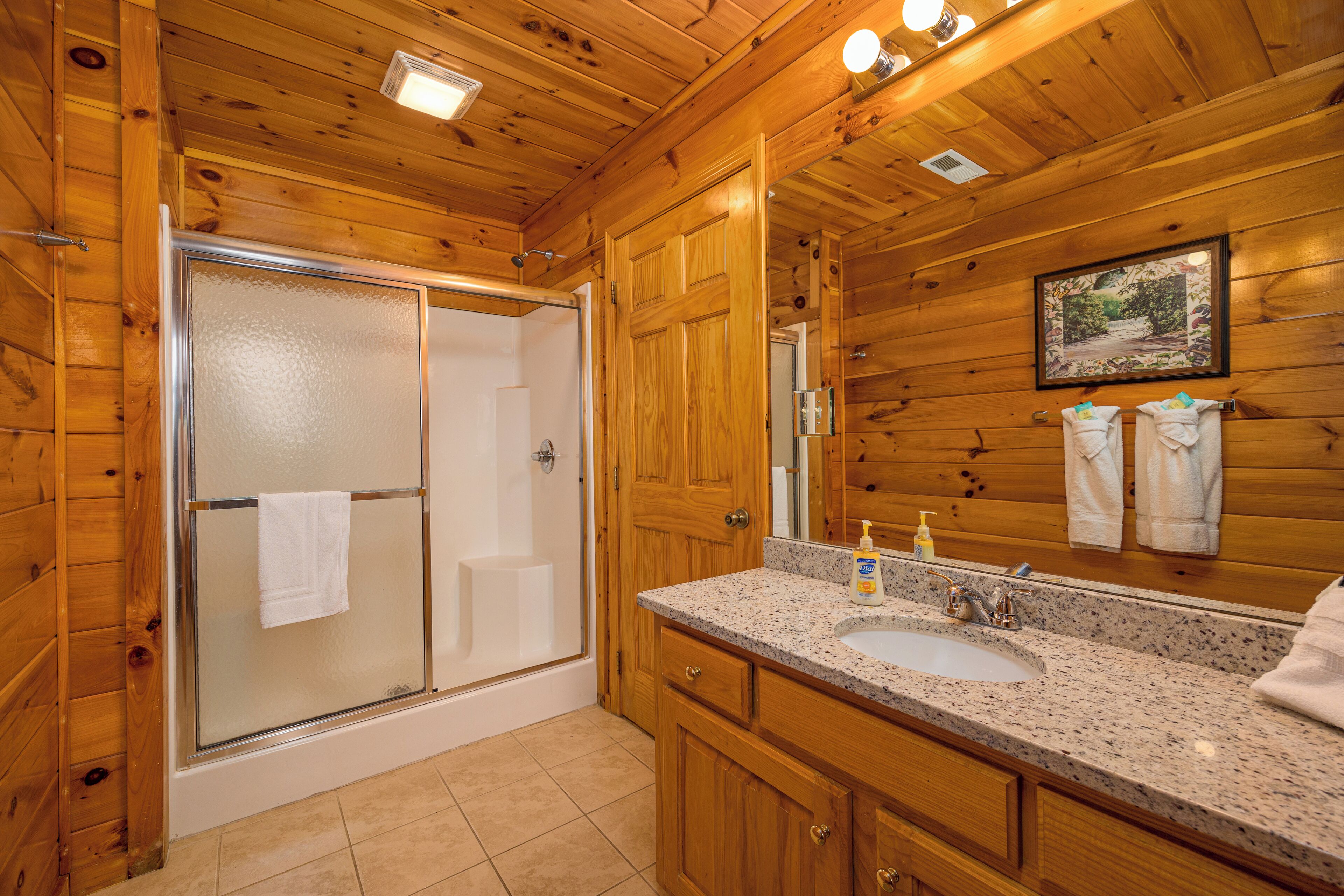 A wooden cabin bathroom with a glass shower enclosure, a sink, and a large mirror.