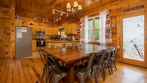 A wooden cabin interior with a dining table, chairs, a refrigerator, a microwave, and a kitchen counter. - Smoky Mountain Lodge | 6 King Suites, Hot Tub, Views, Game Room, flat entry (Sevierville)