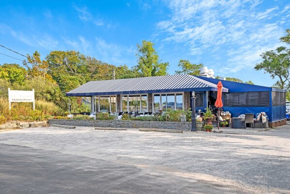 A restaurant with a covered outdoor seating area, a stone wall, and a signboard.