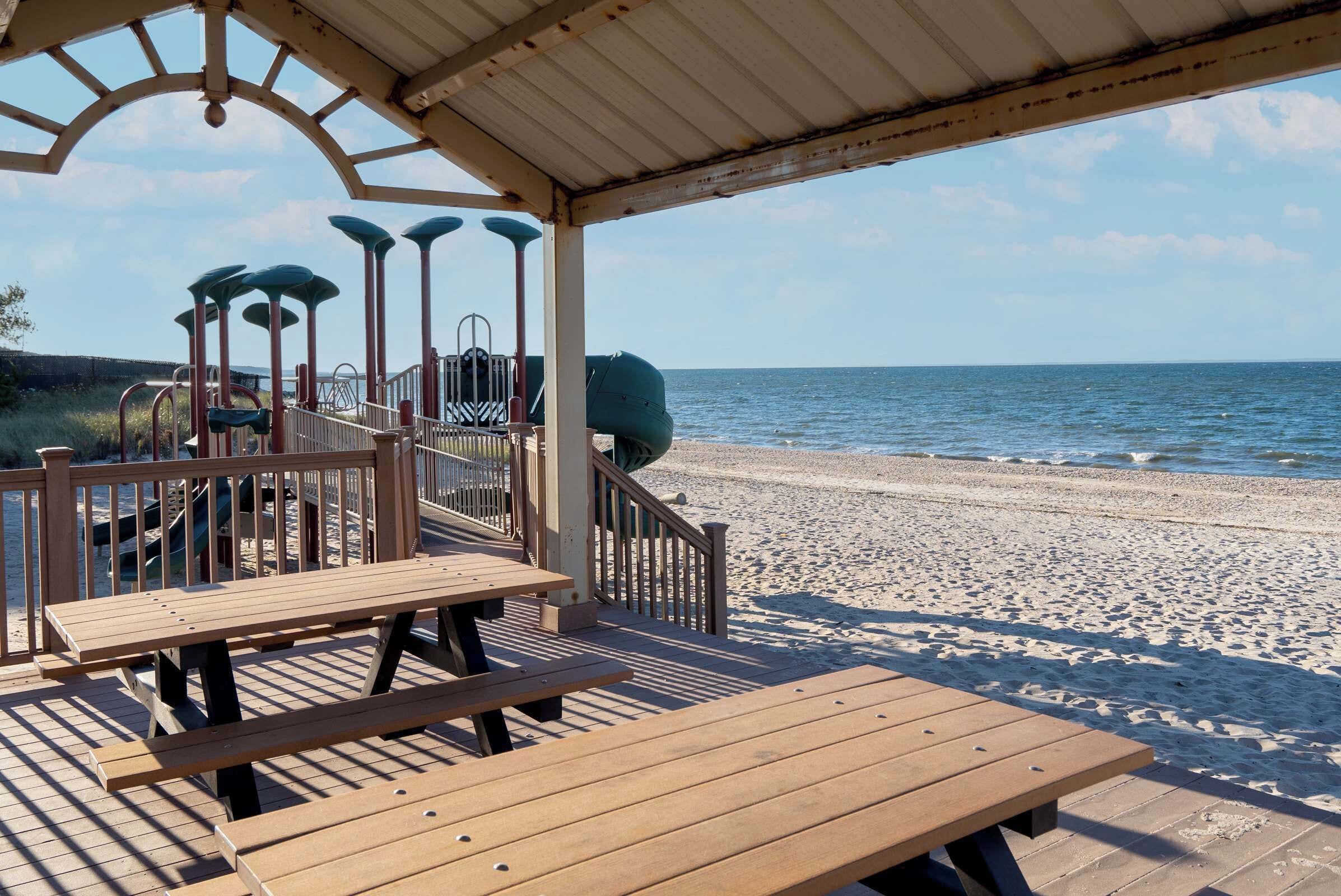 Een houten terras met picknicktafels met uitzicht op een strand.