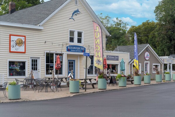 A waterfront building with a blue sign for Blue Water Fish Market and Eatery, outdoor seating, and flags.