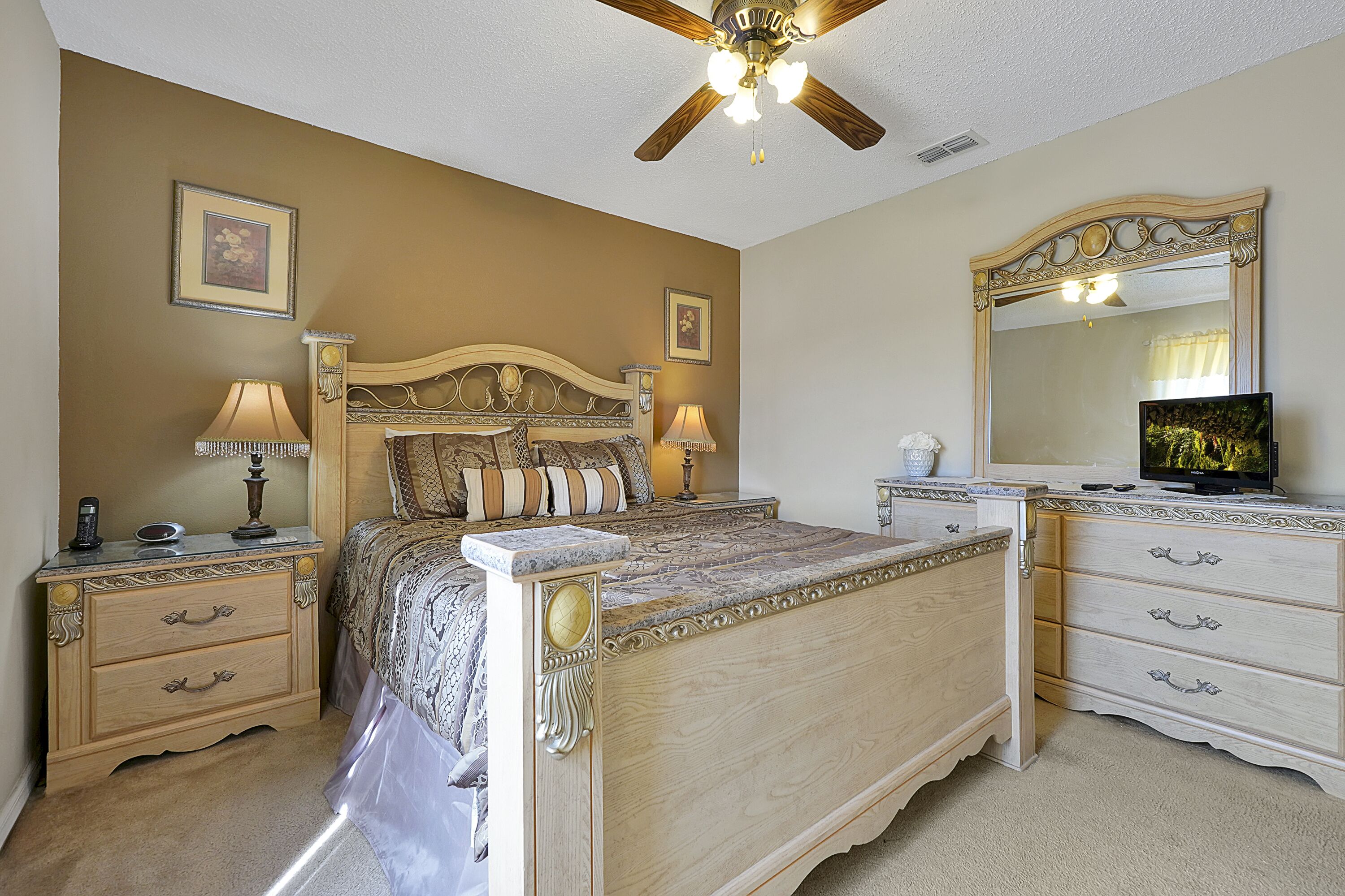 A bedroom with a bed, nightstands, a dresser, a mirror, and a ceiling fan.