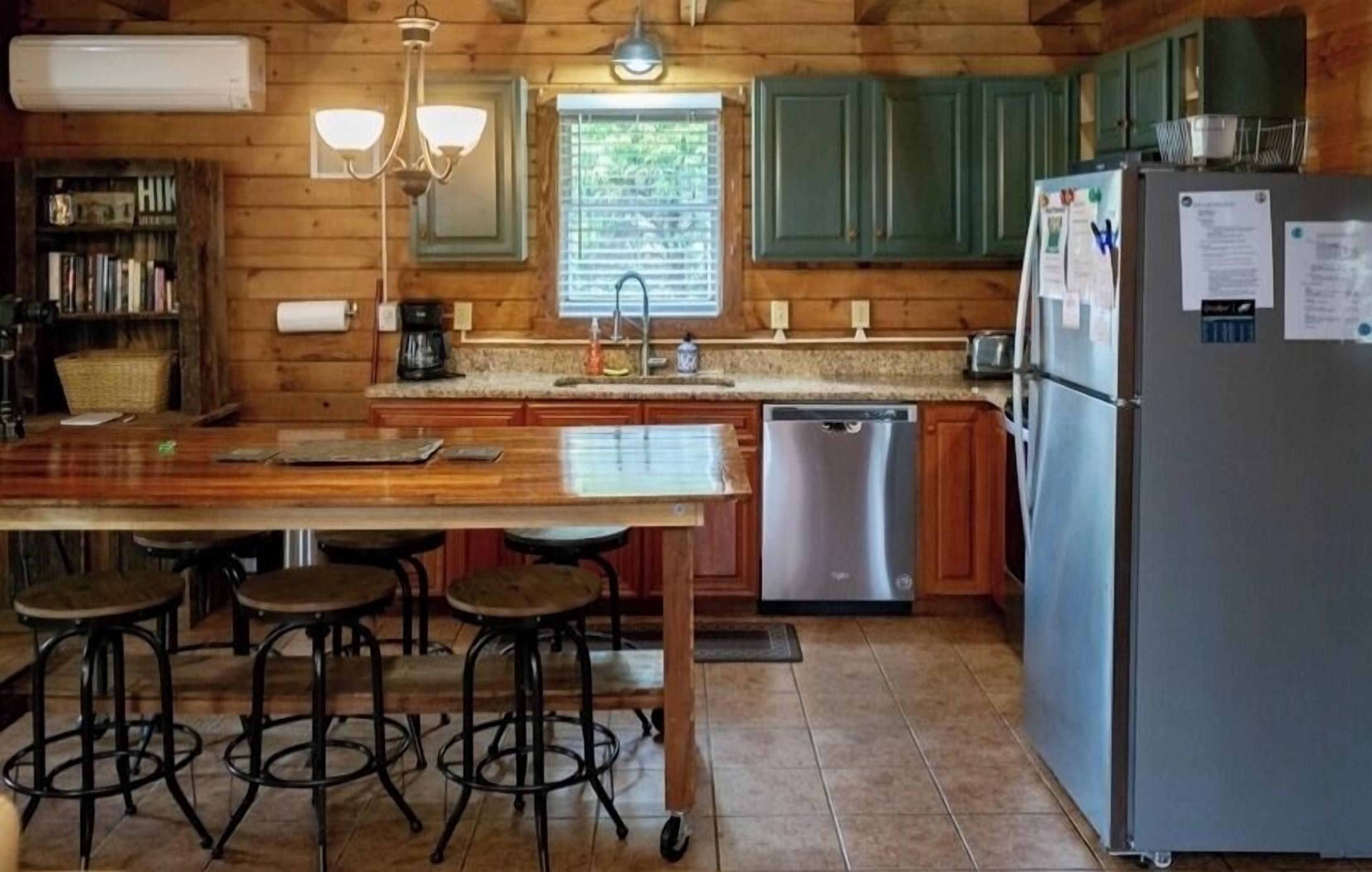 A wooden cabin-style kitchen with a central island, bar stools, a refrigerator, and a window with blinds.
