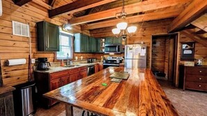 Cocina de cabaña de madera con una isla central grande, armarios empotrados y una lámpara colgante.