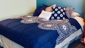A bedroom with a bed, a clock, wall sconces, and a painting. - Waikiki Grand Across from Waikiki Beach & Zoo in the heart of Waikiki! (Honolulu)