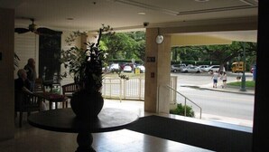 A lobby with a large potted plant, a round table, and a view of the street outside. - Waikiki Grand Across from Waikiki Beach & Zoo in the heart of Waikiki! (Honolulu)
