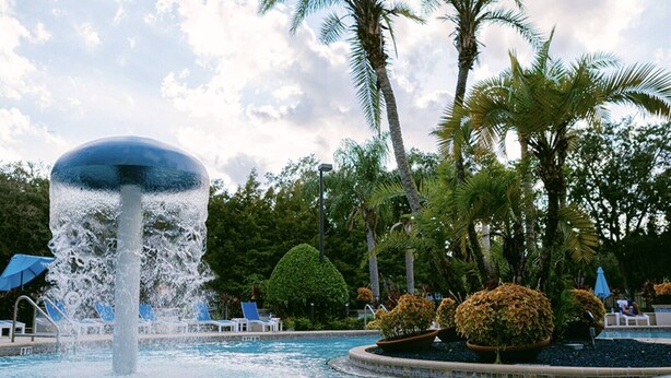 Une fontaine d’eau surmontée d’un grand dôme, entourée de palmiers et de chaises longues.