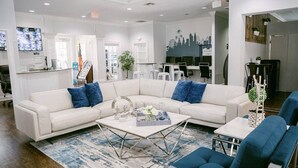 Un hall d’hôtel moderne avec un canapé blanc, des fauteuils bleus, une table basse et une fresque représentant un paysage urbain sur le mur.