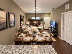 A dining area with a marble countertop, a chandelier, a television, and a sofa.
