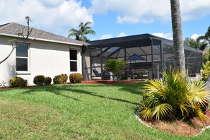 A house with a covered patio, a lawn, and a small garden with palm plants.