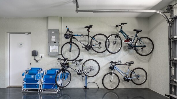 Een schone, overdekte fietsenopslag met meerdere fietsen aan de muur en een blauwe fietsenstandaard op de vloer.