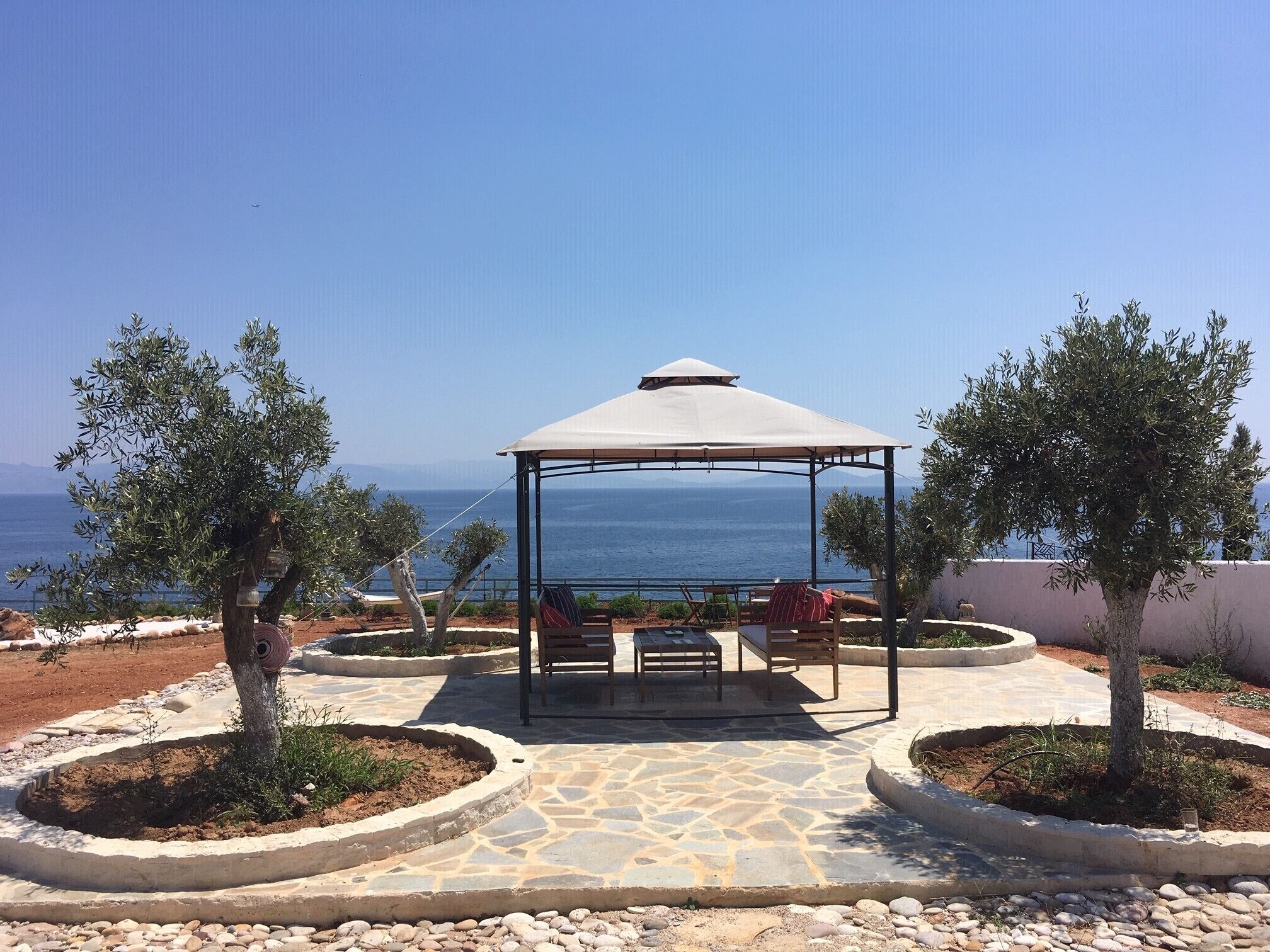 A gazebo with a stone floor and seating, overlooking a coastal view.
