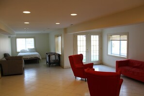 A spacious living room with a bed, a red armchair, and a sofa.
