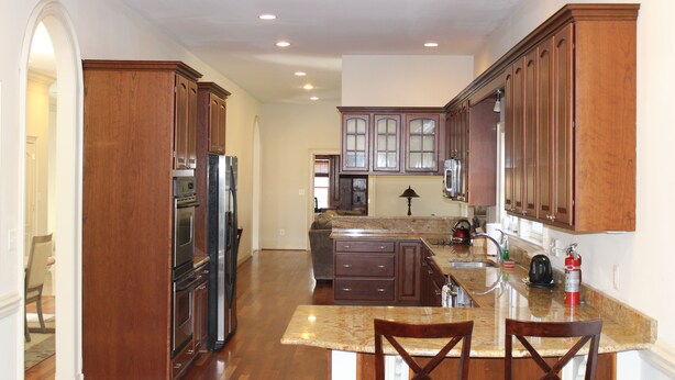 A spacious kitchen with wooden cabinets, a granite countertop, and a central island with bar stools. - Nice Quiet Family Home - Long Term (Potomac)