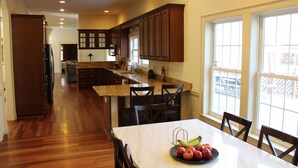 A spacious kitchen with wooden cabinets, a marble countertop, and a dining area with a table set for four. - Nice Quiet Family Home - Long Term (Potomac)