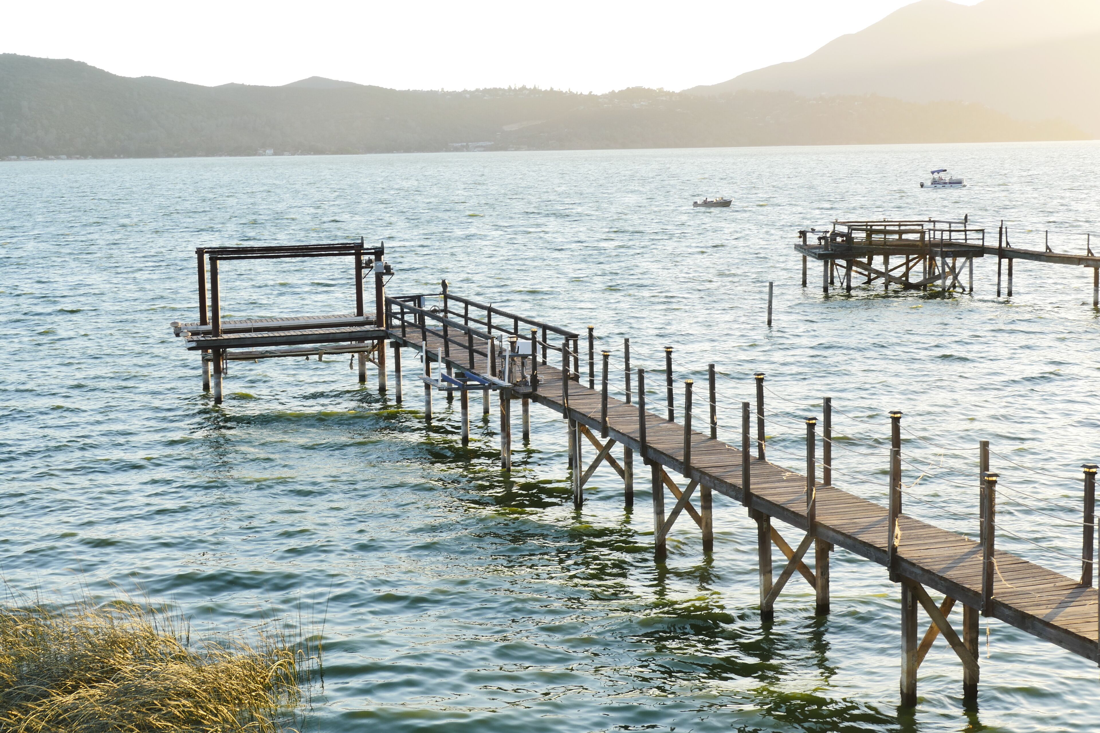 A wooden pier extending into calm water with a bench and a small boat in the distance.