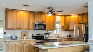 A modern kitchen with wooden cabinets, a central island with stools, a ceiling fan, and built-in appliances. - Downtown home, sleeps 6, pool, free WiFi, walk to Library, Doc's, Eatery (Port Charlotte)