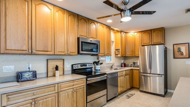 A kitchen with wooden cabinets, stainless steel appliances, a microwave, oven, and a refrigerator. - Downtown home, sleeps 6, pool, free WiFi, walk to Library, Doc's, Eatery (Port Charlotte)