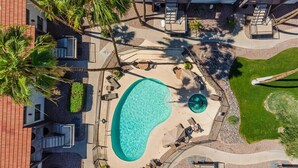 An aerial view of a hotel with a swimming pool, palm trees, and a well-maintained lawn.