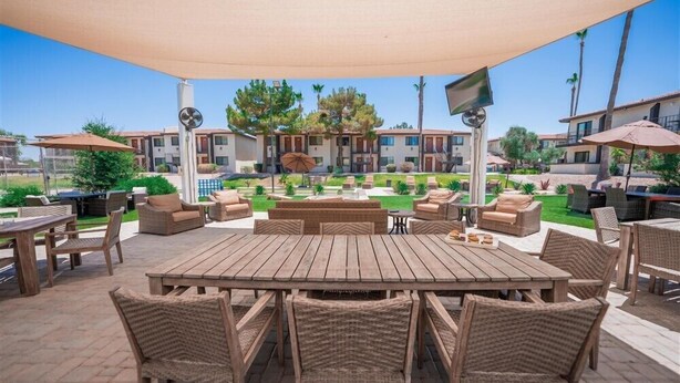 An outdoor patio area with a wooden table and wicker chairs, surrounded by lounge chairs and umbrellas. - 141 Fully Furnished, WiFi Included! (Scottsdale)