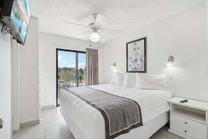 Une chambre avec un lit, un ventilateur de plafond, une télévision, un tableau et un balcon avec vue.